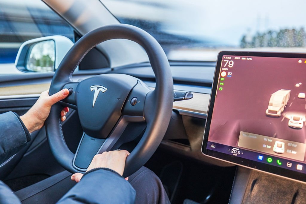 Close up view of female hands on Tesla Model Y steering wheel with autopilot screen showing road traffic