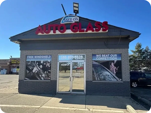 Exterior view of the Save On Auto Glass shop located at 43917 Van Dyke Ave, Sterling Heights, MI, displaying promotional signs for free windshield replacement and competitive pricing.