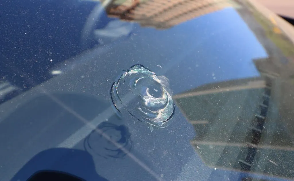 Close-up of a car windshield with a circular bullseye chip caused by impact, showing localized glass damage that may require professional windshield repair to prevent cracking.