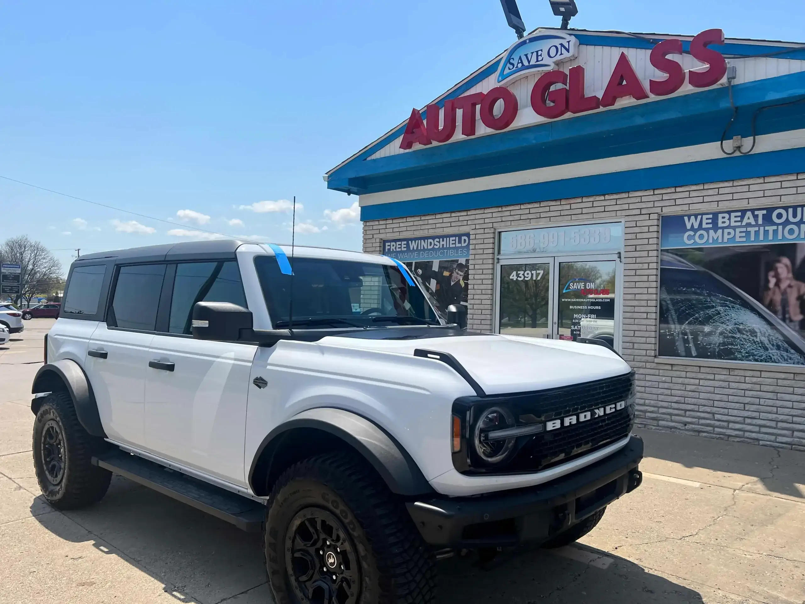A white car stands in front of the save on auto glass shop