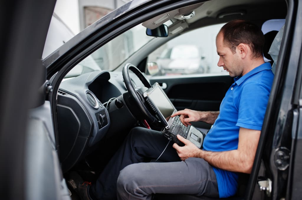 Car repair and maintenance theme. Electric mechanic in uniform working in auto service, making car diagnostics using obd device with laptop.
