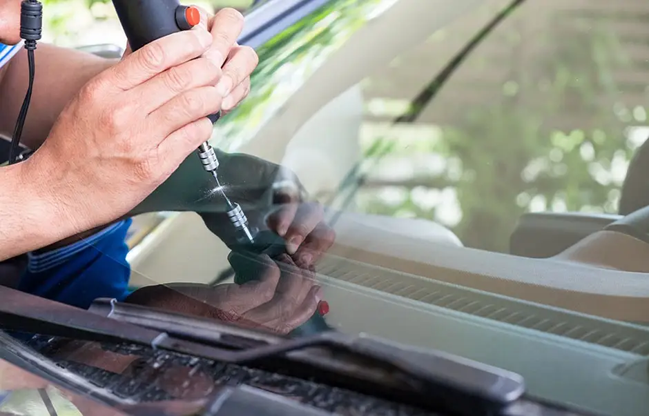 Technician repairing a chip in a vehicle windshield using a windshield repair tool.