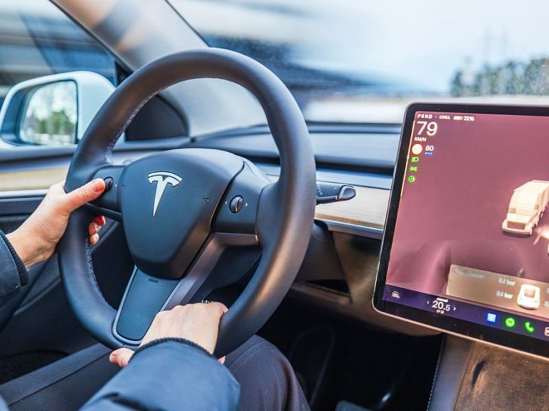 Close up view of female hands on Tesla Model Y steering wheel with autopilot screen showing road traffic