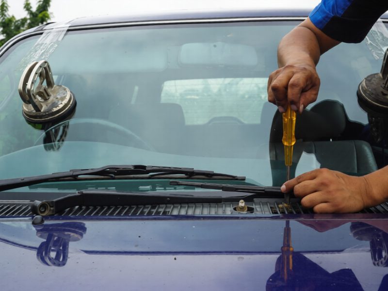 Glazier using tools repairing to fix crack broken windshield on the front window glass