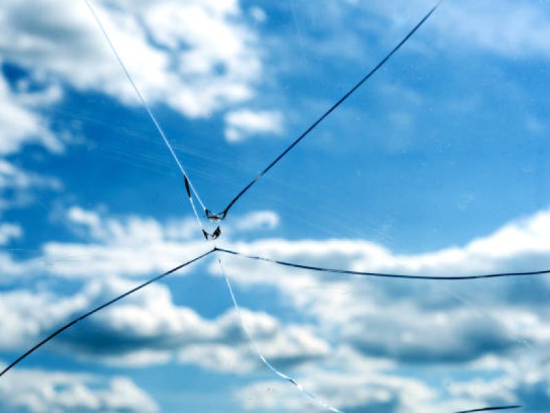 Single accurate cracked glass window with a blue sky background and white summer clouds